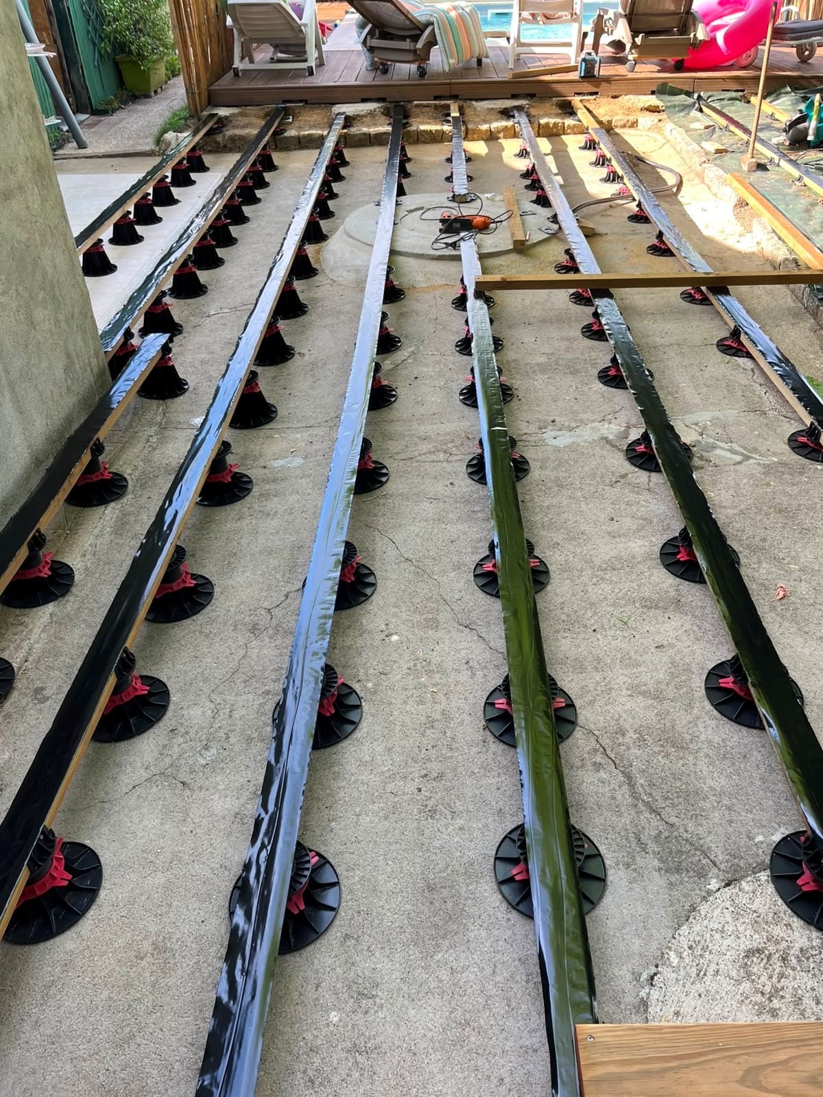 Lambourdes sur plots réglables noirs et rouges pour l'installation d'une terrasse en bois sur dalle béton.
