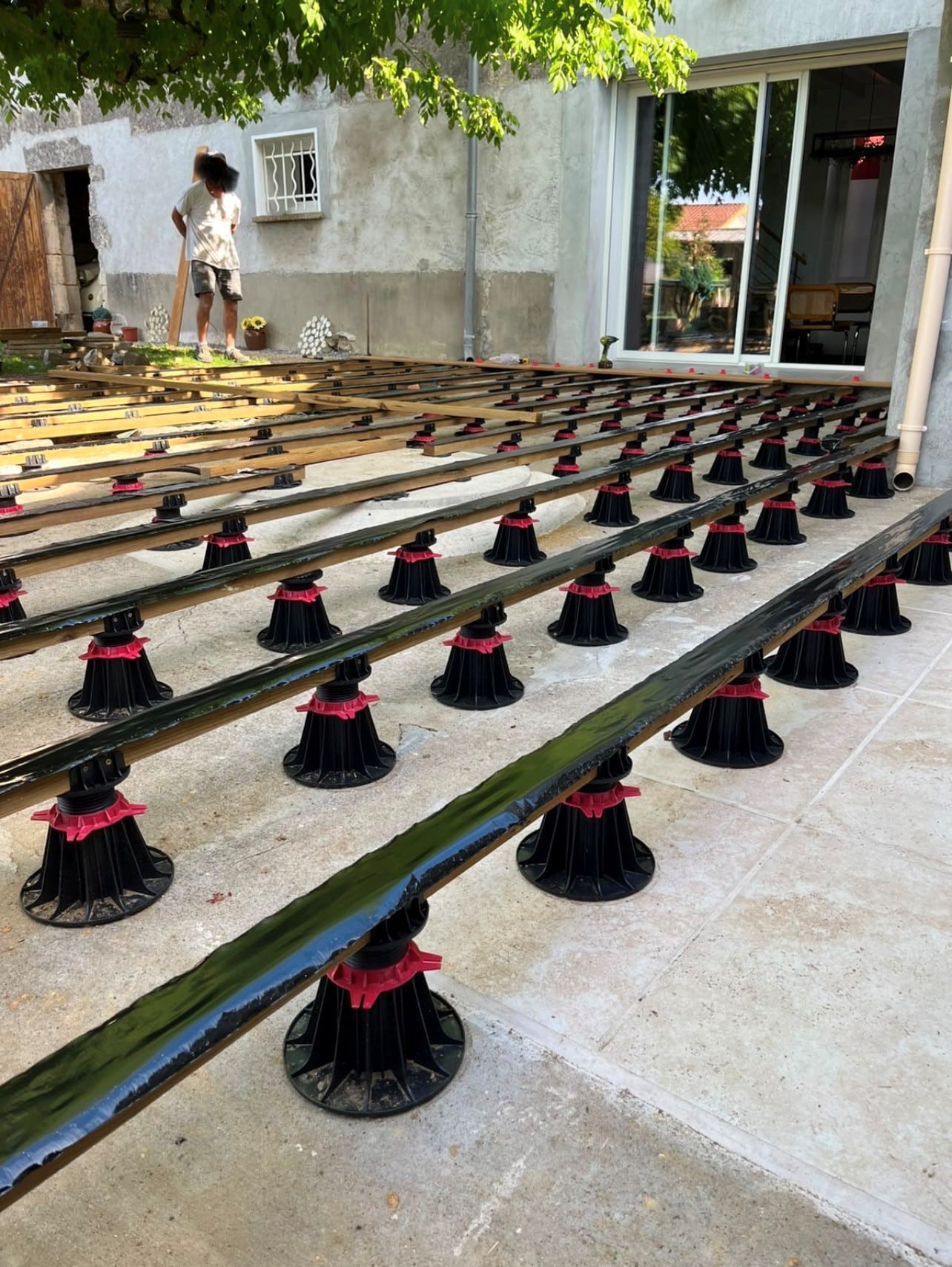 Lambourdes sur plots réglables installées sur une dalle béton pour la structure d'une terrasse en bois.